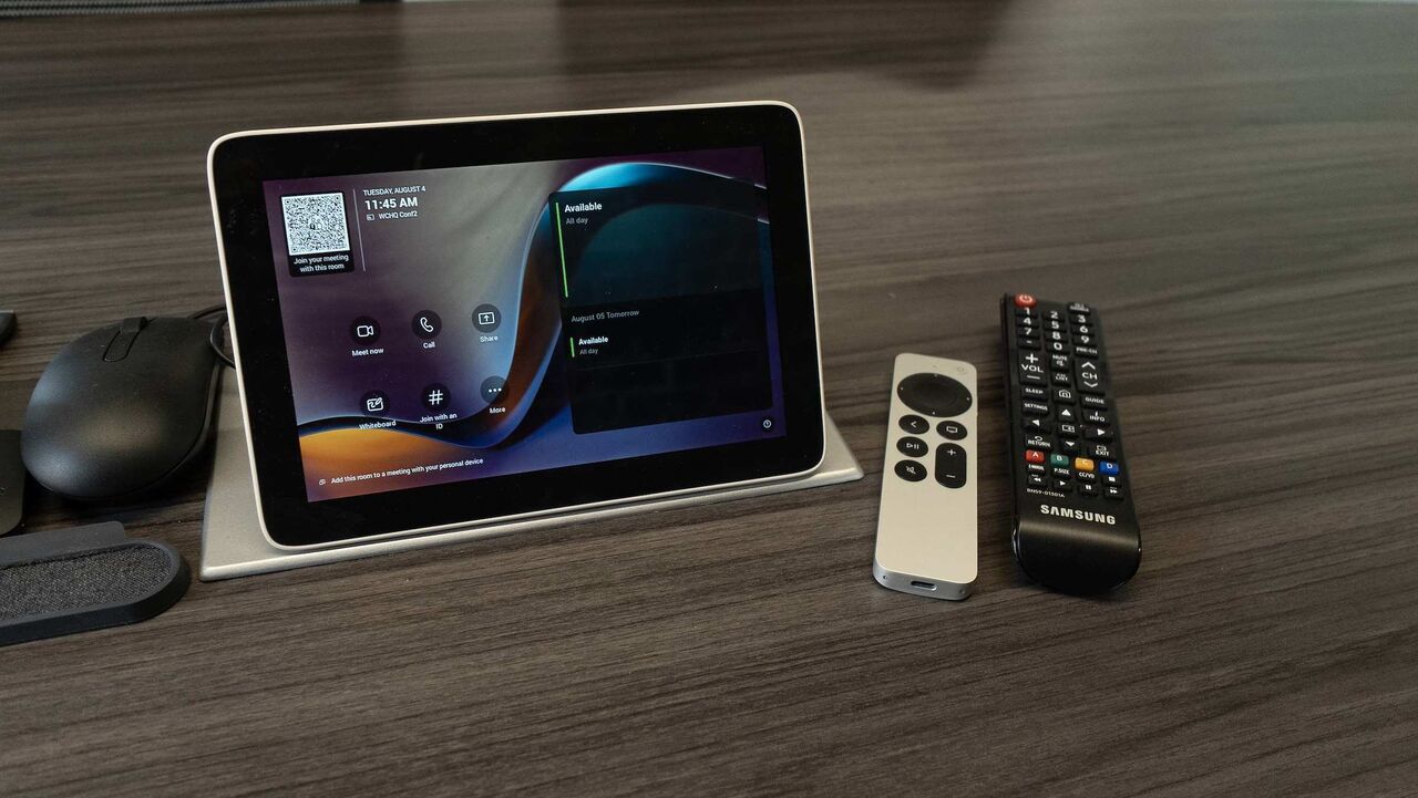 The conference room touch control panel on the table, beside a mouse and the display remotes