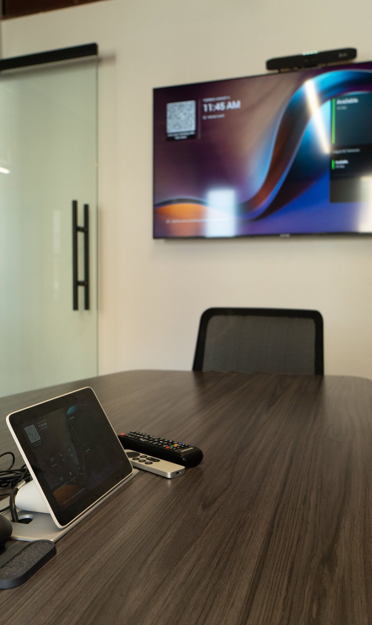 The conference room display and video bar on the wall above the table, with the touch control panel on the table