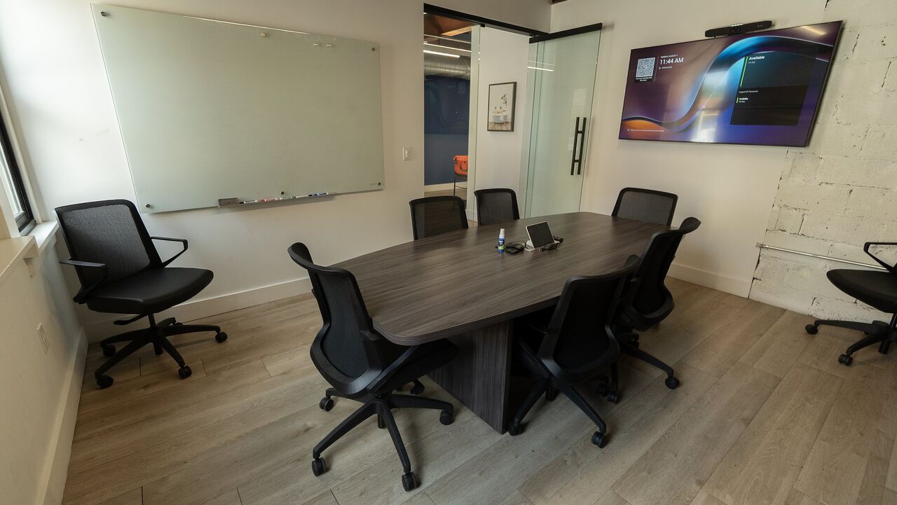 The conference room from the corner: the meeting table and chairs, a wall-length whiteboard, the display and the glass door