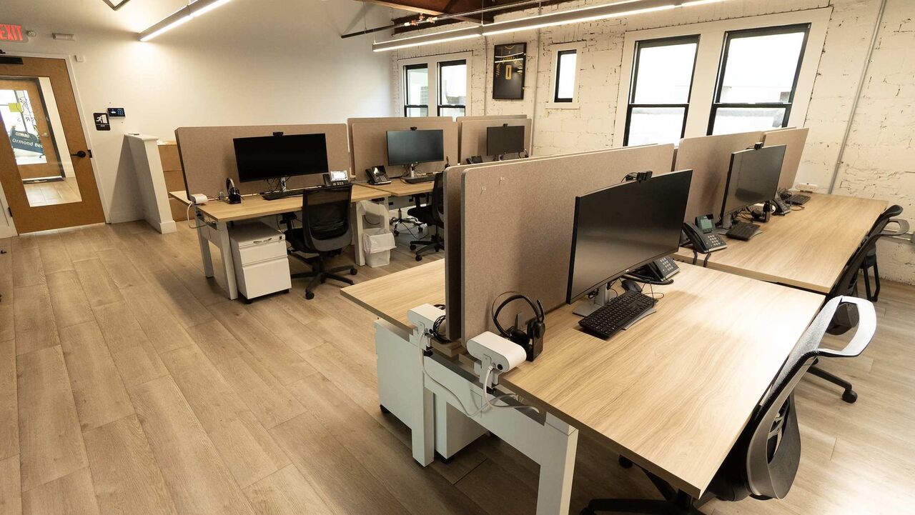 Sit-stand desks with monitors beside the tall street-side windows, under the timber ceiling